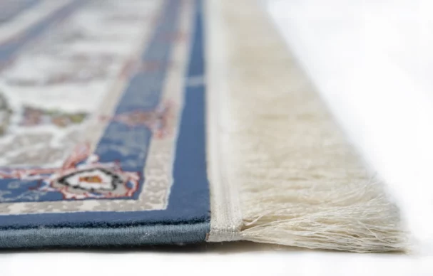 A close-up of a Qaleen Carpets rug's edge, featuring a blue and white border with a patterned design, with a focus on the