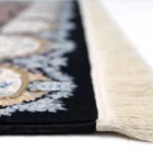 A close-up of a Qaleen Carpets rug with a black and white pattern, featuring a fringe of white and a central design of blue
