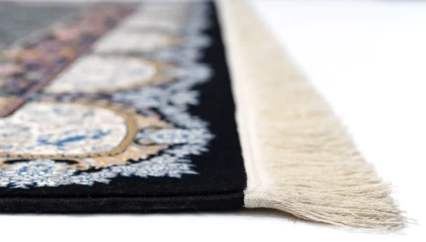 A close-up of a Qaleen Carpets rug with a black and white pattern, featuring a fringe of white and a central design of blue