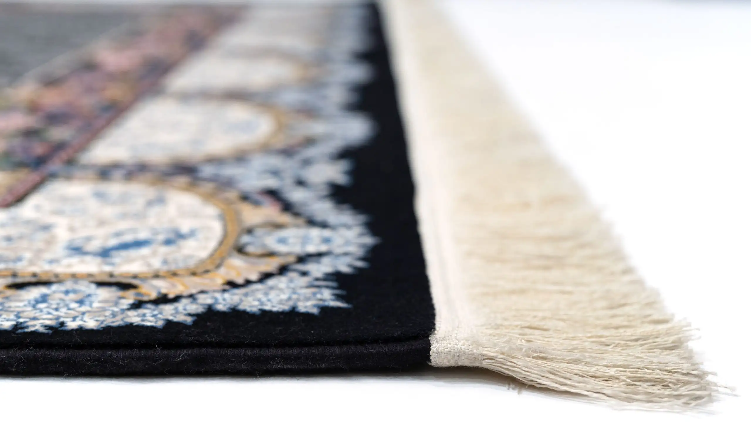 A close-up of a Qaleen Carpets rug with a black and white pattern, featuring a fringe of white and a central design of blue