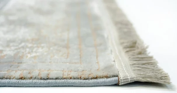 A close-up of a white and gold rug with a subtle, intricate design, made by Qaleen Carpets, showcasing their expertise in