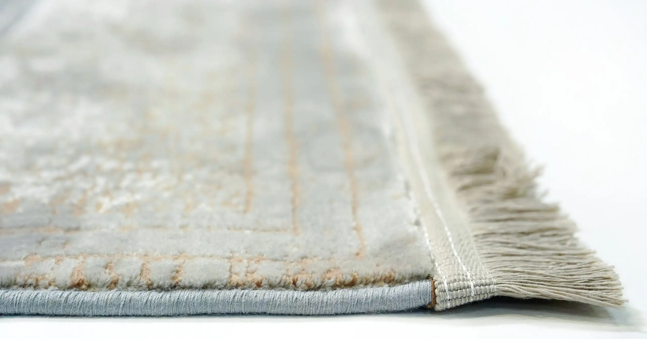 A close-up of a white and gold rug with a subtle, intricate design, made by Qaleen Carpets, showcasing their expertise in