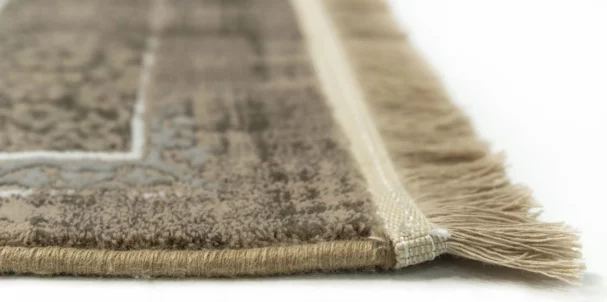 A close-up of a rug's edge, with a focus on the fringe and the soft, plush carpeting, made by Qaleen Carpets