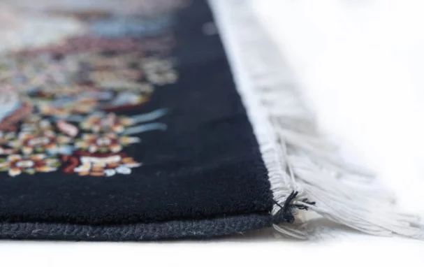 A close-up of a Qaleen Carpets rug's edge, with a focus on the intricate design and the soft, white fringe