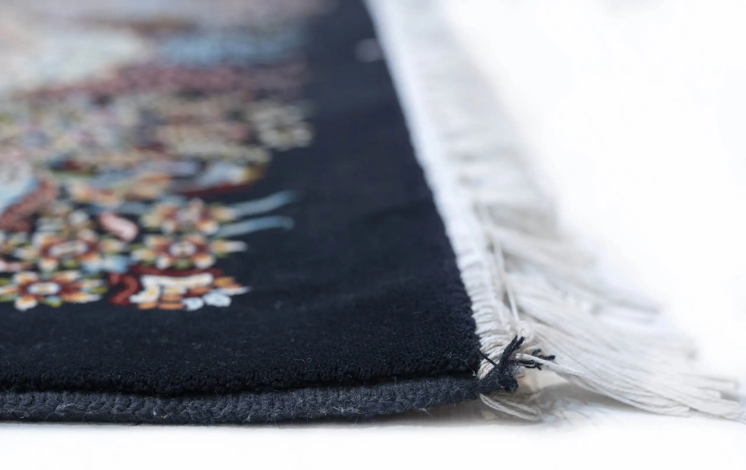 A close-up of a Qaleen Carpets rug's edge, with a focus on the intricate design and the soft, white fringe