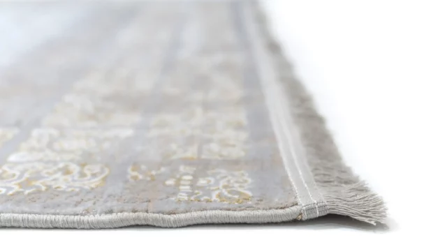 A close-up of a Qaleen Carpets rug with a soft, white, and gold pattern, featuring a delicate, intricate design