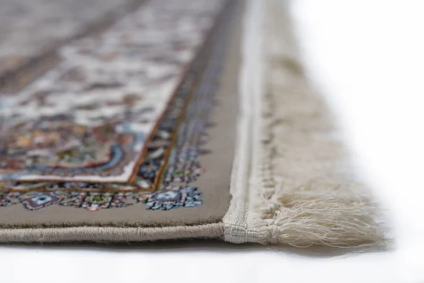 A close-up of a Qaleen Carpets rug with intricate patterns and a fringe on the edge, showcasing its high-quality
