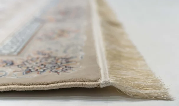 A close-up of a Qaleen Carpets rug's edge, with its intricate design and fringes on a white background