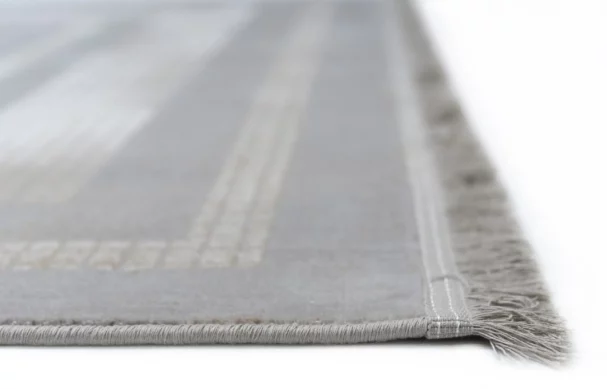 A close-up of a light grey and white striped rug with a subtle fringe on the edge, made by Qaleen Carpets