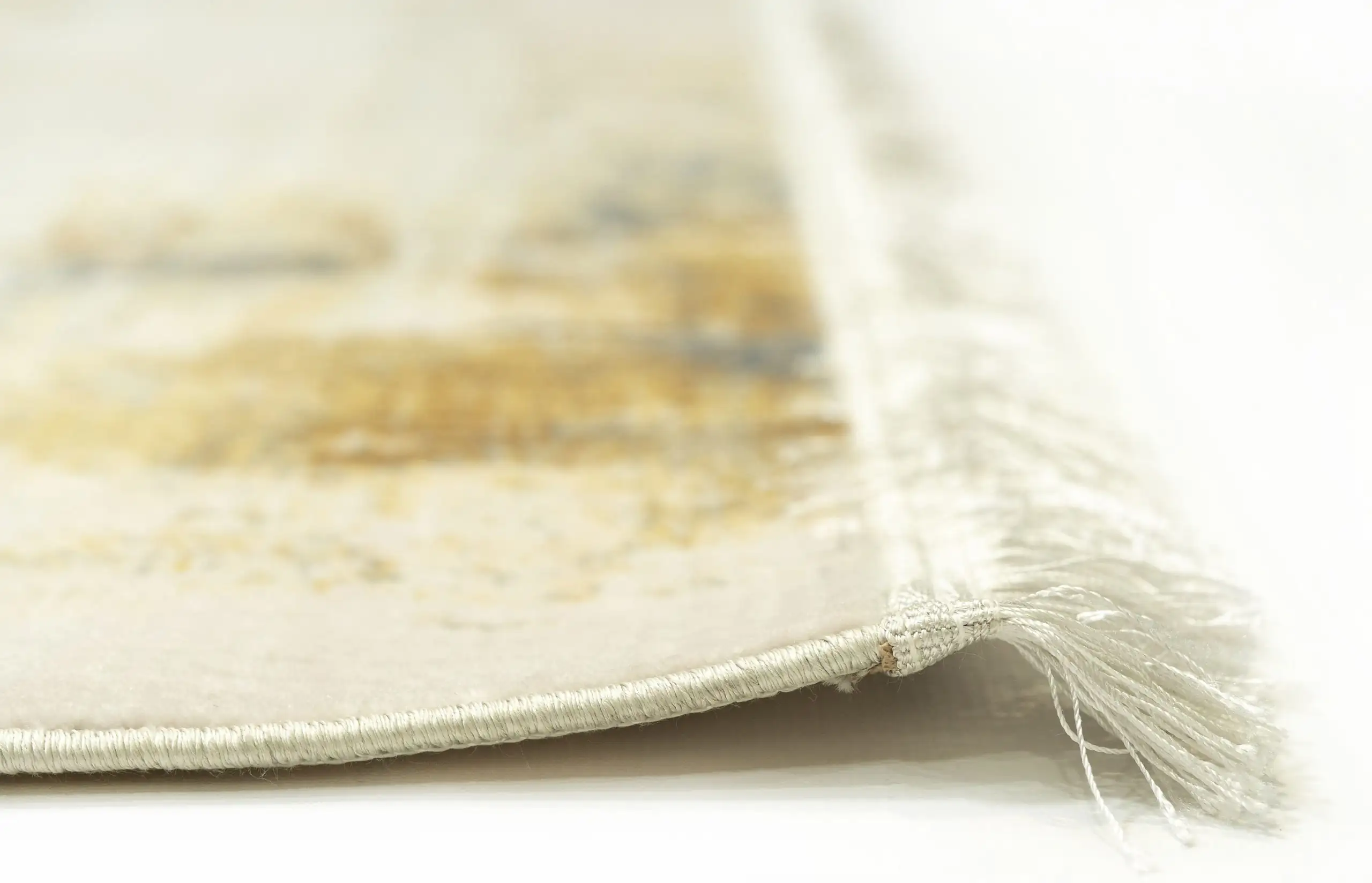 A close-up of a Qaleen Carpets rug's edge, with a focus on the intricate weaving and the soft, white and gold colors of the