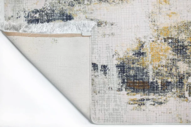 A close-up of a rug's corner, with a white, gold, and dark blue pattern, with a white fringe at the edge, from Qaleen Carpets