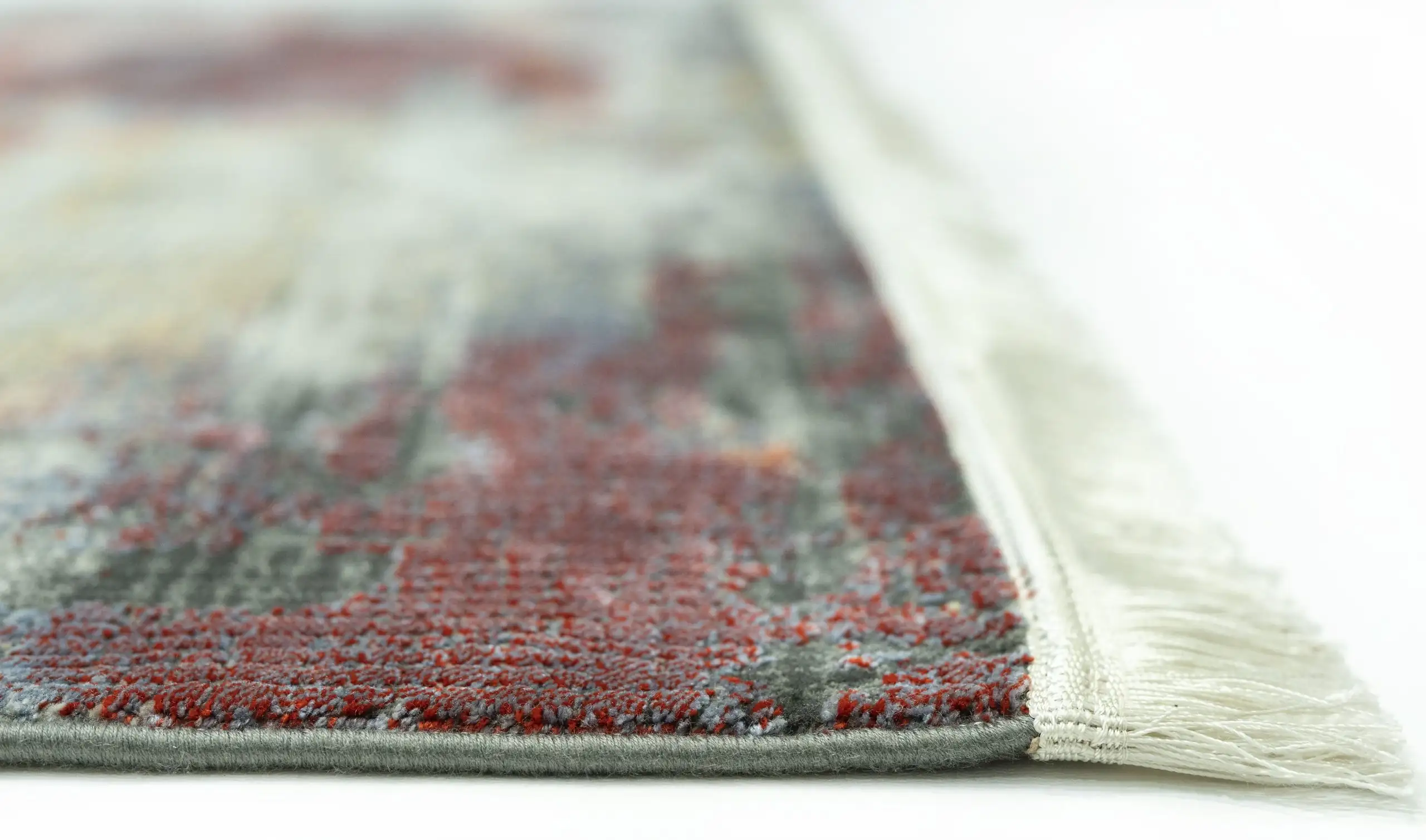 A close-up of a rug with a vibrant, intricate design, made by Qaleen Carpets, with a focus on the edge of the rug's fringe
