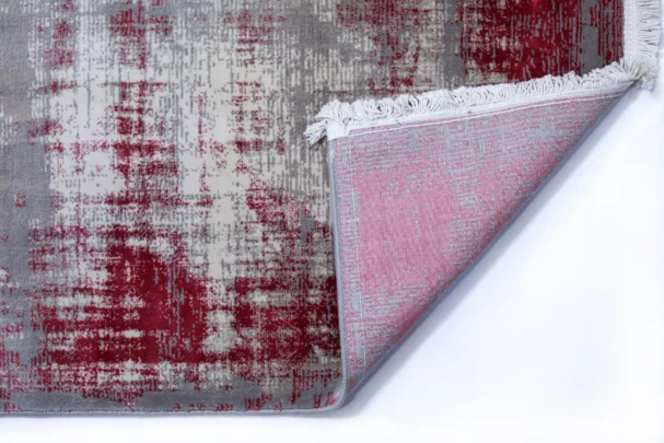 Qaleen Carpets A close-up of a rug with a red and grey pattern, with a corner folded over to show the underside, featuring a