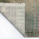 A close-up of a rug's corner, with a fringe of white yarn and a pattern of interlocking squares in various shades of green