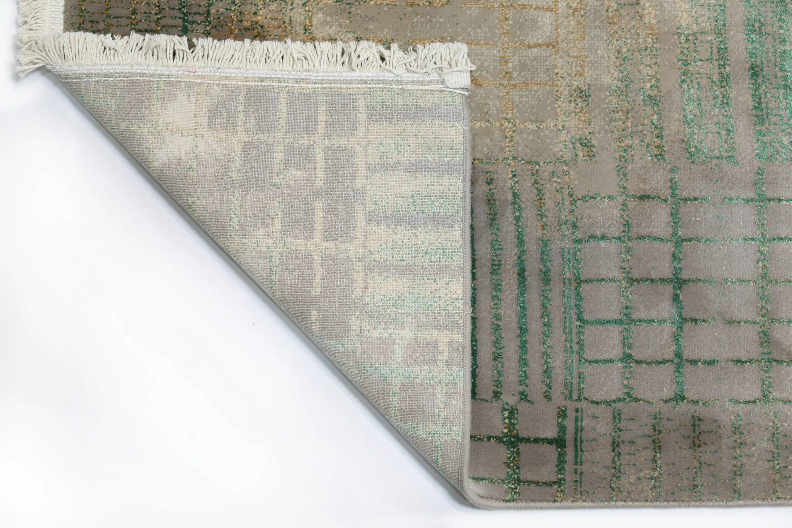 A close-up of a rug's corner, with a fringe of white yarn and a pattern of interlocking squares in various shades of green