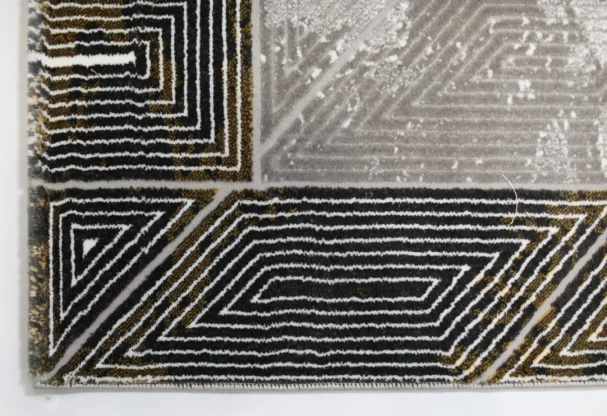 A close-up of a Qaleen Carpets rug, featuring a black and gold pattern with a white background