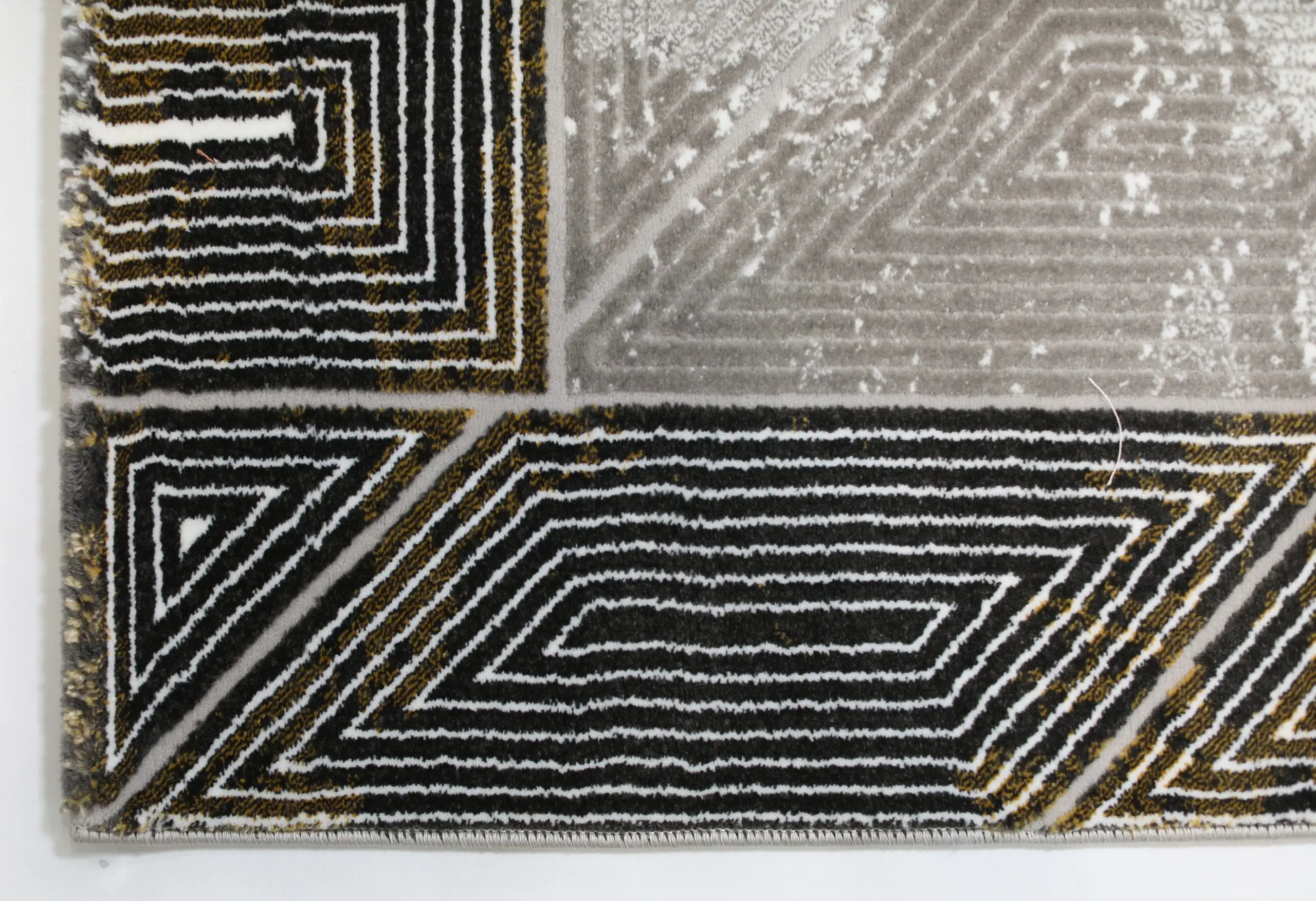 A close-up of a Qaleen Carpets rug, featuring a black and gold pattern with a white background