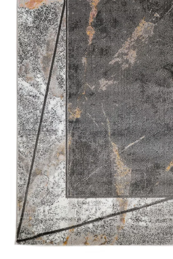 A close-up of a Qaleen Carpets rug with a mix of grey, white, and gold patterns, featuring a central grey rectangle with a