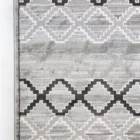 A close-up of a gray and white rug with a repeating pattern of interlocking shapes, made by Qaleen Carpets