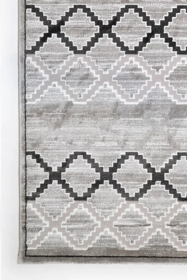 A close-up of a gray and white rug with a repeating pattern of interlocking shapes, made by Qaleen Carpets