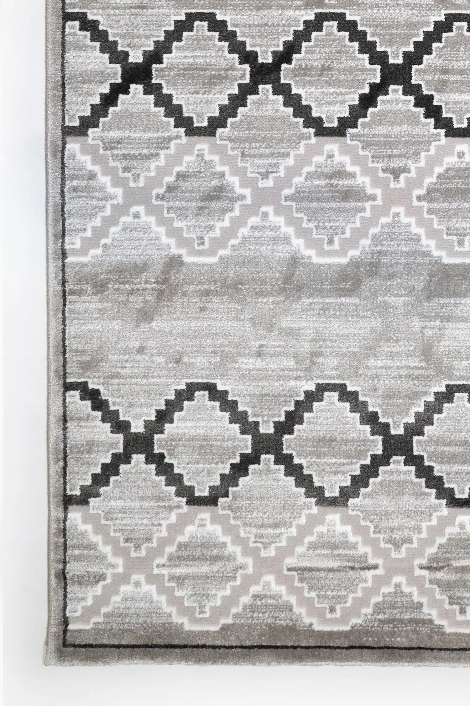 A close-up of a gray and white rug with a repeating pattern of interlocking shapes, made by Qaleen Carpets