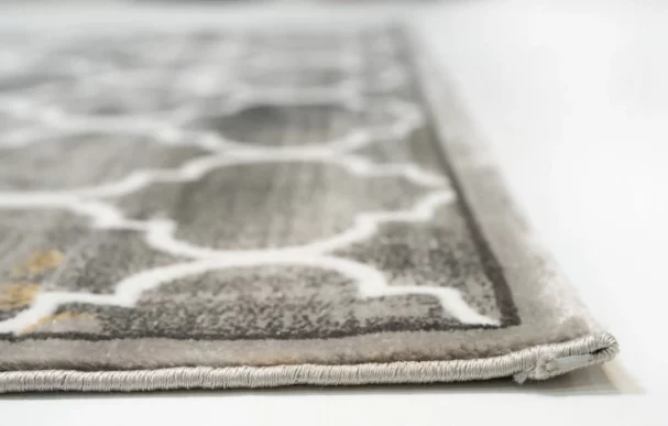 A close-up of a grey and white patterned rug with a thick, plush pile, made by Qaleen Carpets, with a focus on the rug's