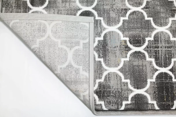 Qaleen Carpets A close-up of a gray and white patterned rug with a corner folded up, showcasing its intricate design and