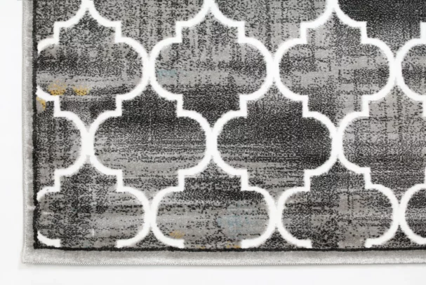 A close-up of a gray and white patterned rug with a Qaleen Carpets design, featuring a repeating pattern of interconnected