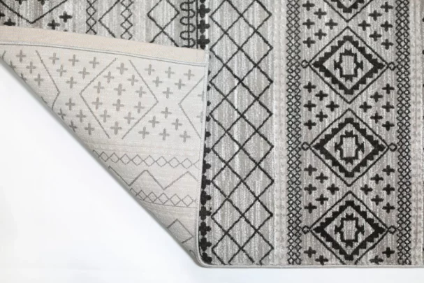 Qaleen Carpets A close-up of a rug's corner, with a pattern of geometric shapes and a neutral color palette