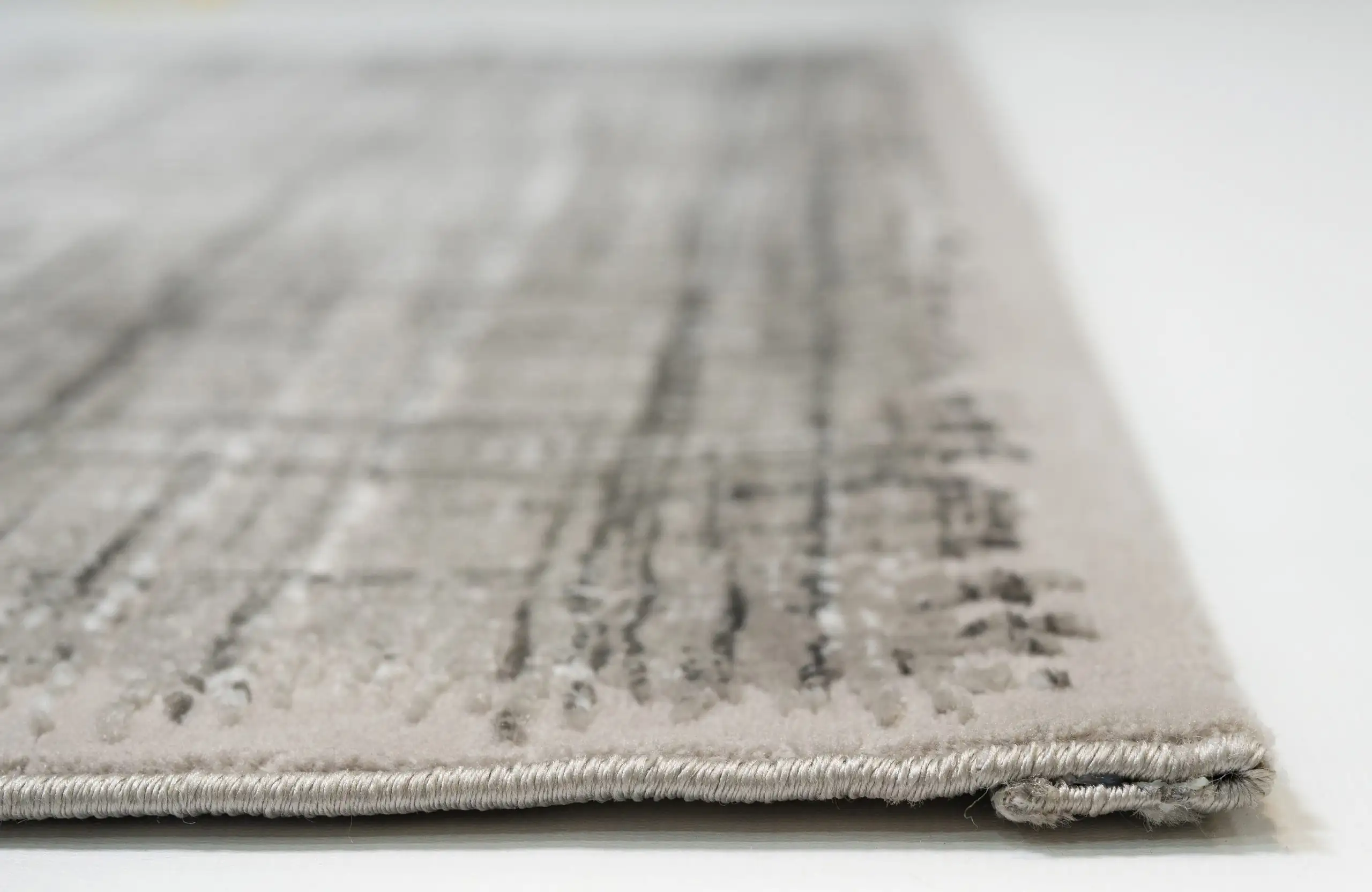 A close-up of a light grey and white woven carpet with a subtle, intricate pattern, made by Qaleen Carpets
