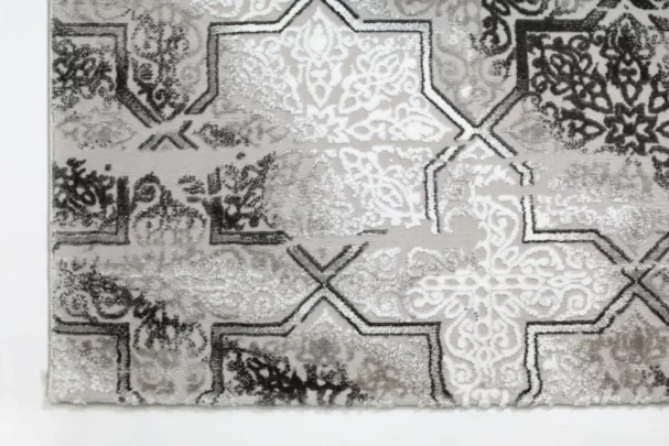 A close-up of a Qaleen Carpets rug with a repeating pattern of intricate, ornate designs in a mix of white, grey, and black,