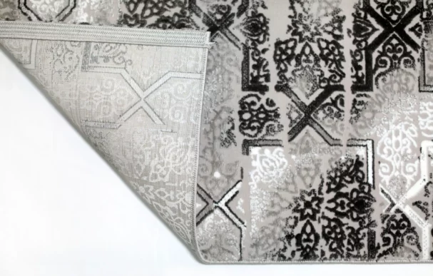 A close-up of a Qaleen Carpets rug with a white and black pattern, with a corner folded over to show the rug's edge and a