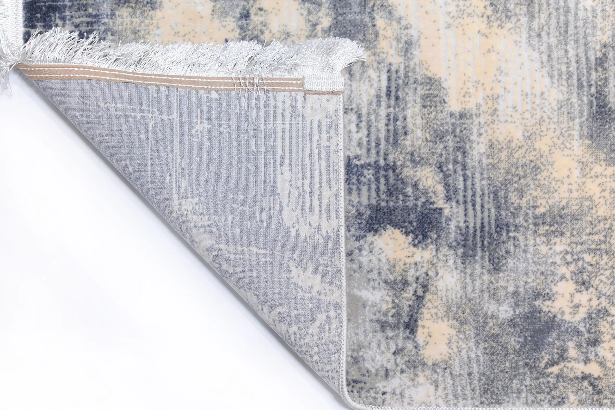 A close-up of a Qaleen Carpets rug's edge, with a subtle pattern and soft, white fringe