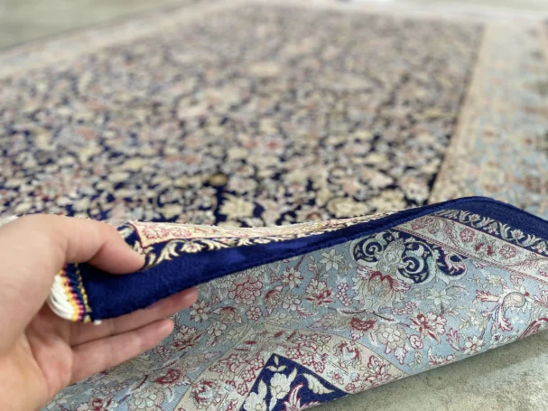 Carpets A person's hand holding the edge of a beautiful, intricately designed carpet, with a focus on the carpet's intricate