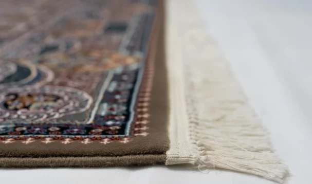 A close-up of a Qaleen Carpets rug with intricate patterns and a fringe of white, set against a white background
