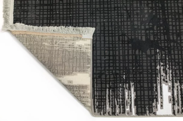 Qaleen Carpets A close-up view of a black and white rug with a fringe border, featuring a grid pattern and a corner turned
