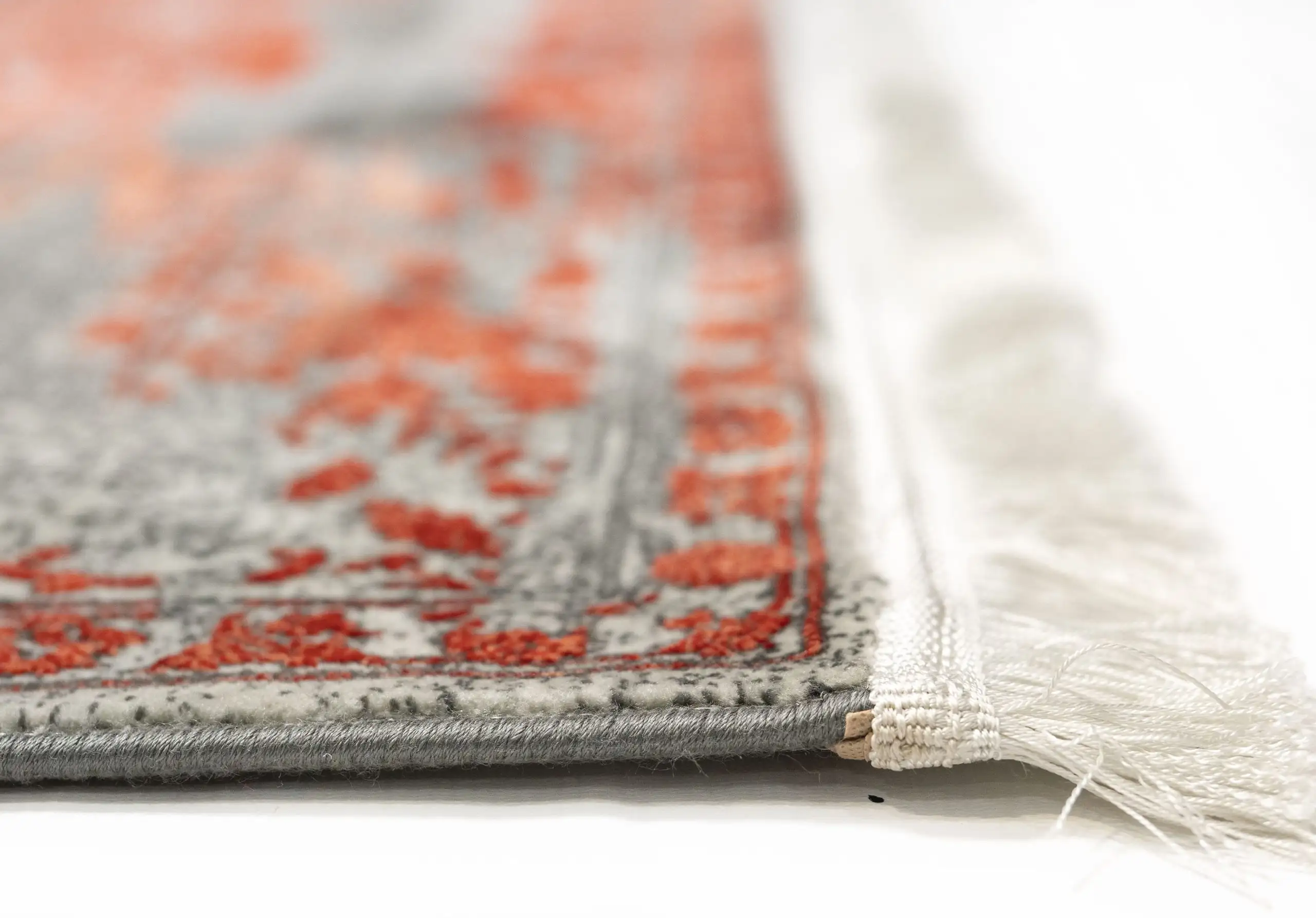A close-up of a rug's edge, with a focus on the intricate pattern and the frayed, white, and red-tinged edges, made by