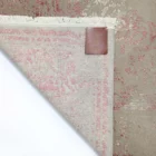 A close-up of a Qaleen Carpets rug's corner, with a small leather tag and frayed edges, on a white background