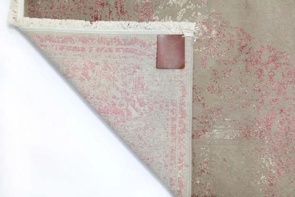 A close-up of a Qaleen Carpets rug's corner, with a small leather tag and frayed edges, on a white background