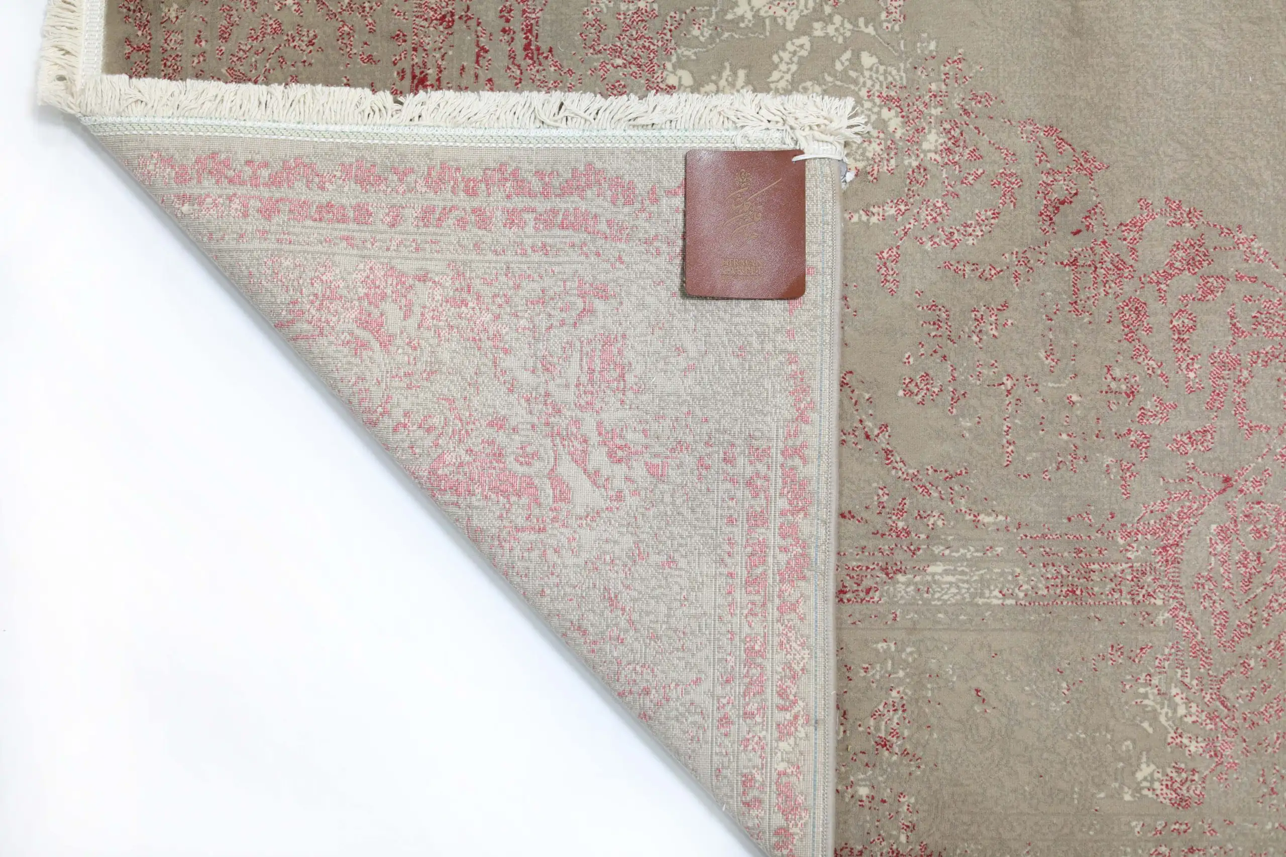 A close-up of a Qaleen Carpets rug's corner, with a small leather tag and frayed edges, on a white background
