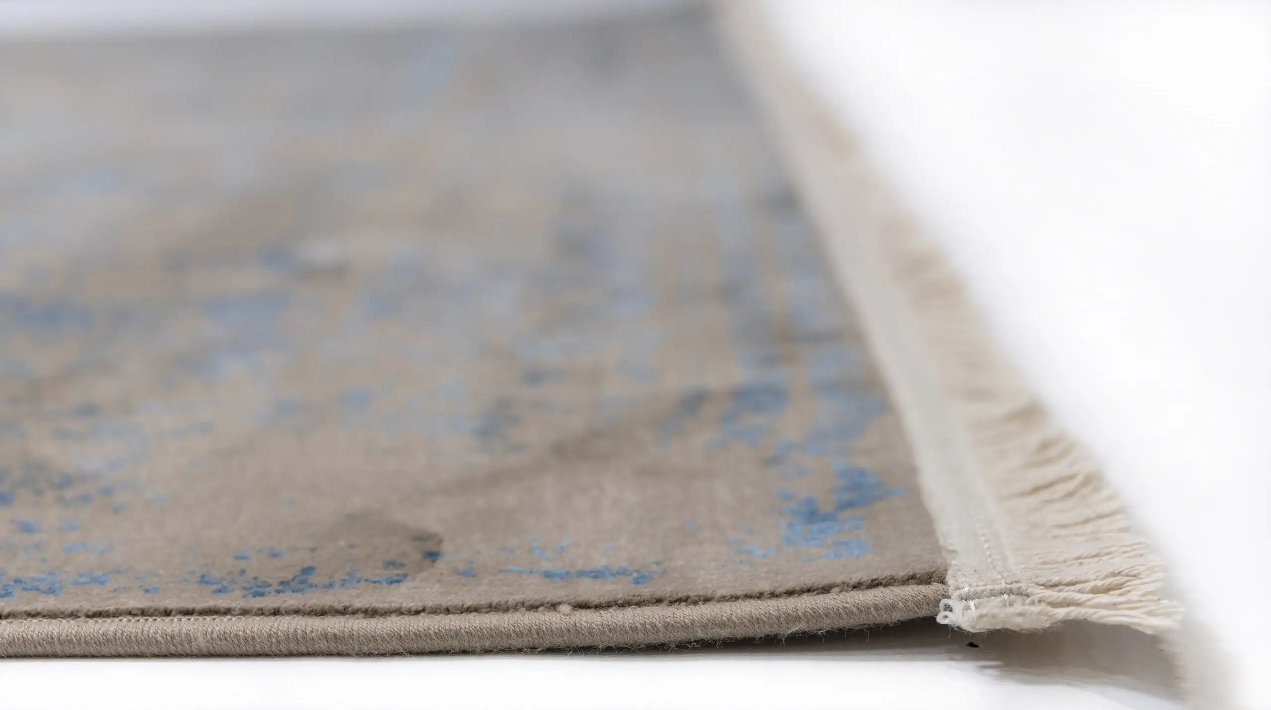 A close-up of a Qaleen Carpets rug's edge, with a focus on the fringe and the carpet's design, showcasing its quality and