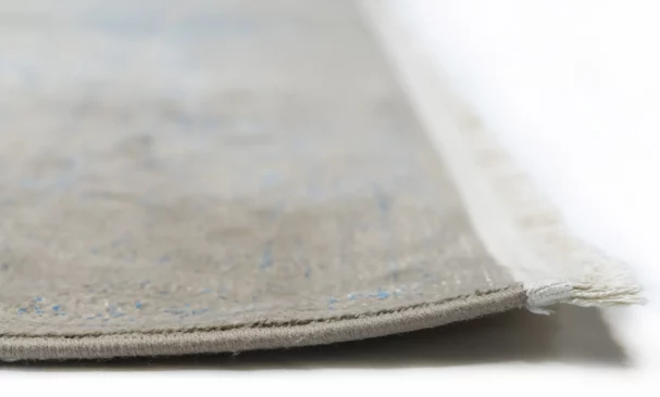A close-up of a Qaleen Carpets rug's edge, with a focus on the intricate weave and the soft, natural color of the carpet's
