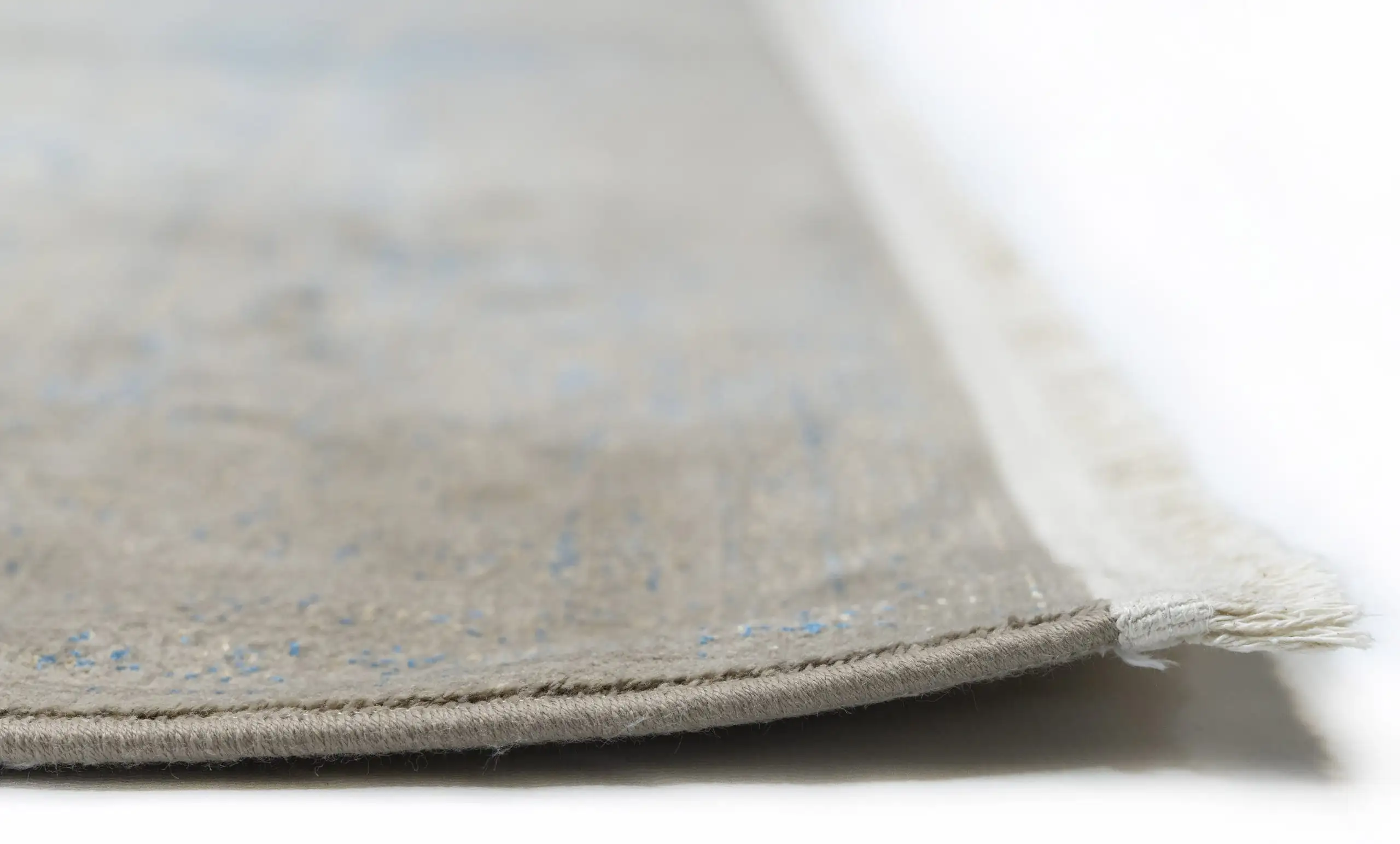 A close-up of a Qaleen Carpets rug's edge, with a focus on the intricate weave and the soft, natural color of the carpet's