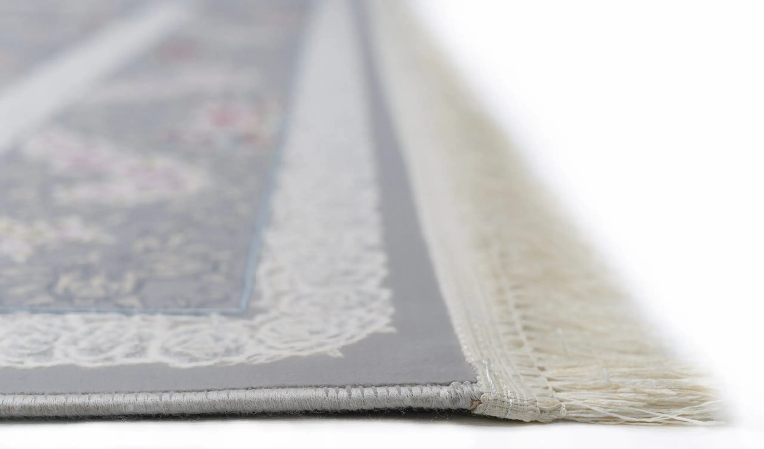 A close-up of a Qaleen Carpets rug with a white border and fringe, featuring a central design in a muted color palette