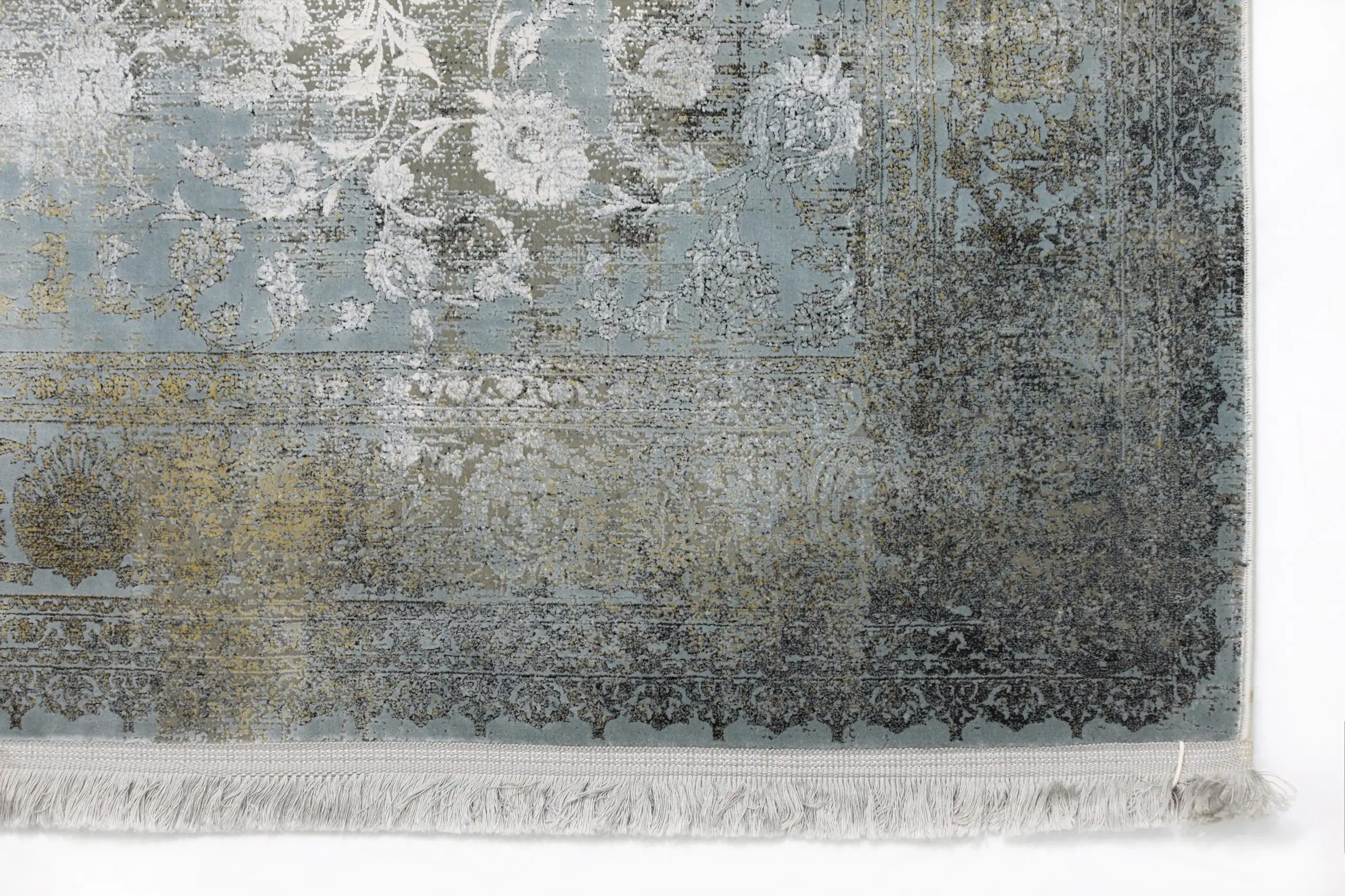 Qaleen Carpets A close-up of a rug with a light blue and gold pattern, with a white fringe at the bottom