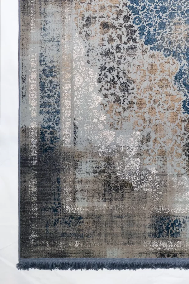 Qaleen Carpets A close-up of a rug with a mix of blue, white, and brown patterns, with a frayed blue edge and a white