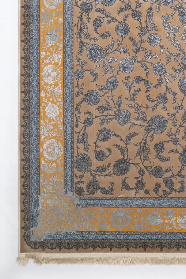 A close-up of a Qaleen Carpets rug with a floral pattern, featuring a mix of blue, gold, and white colors on a tan background