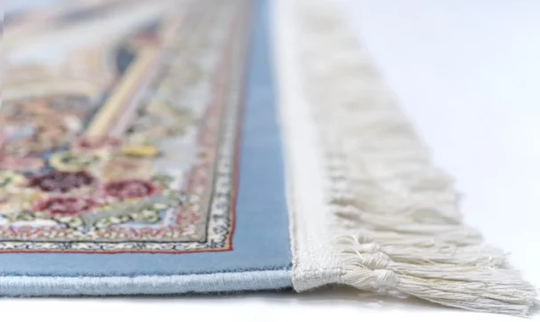 A close-up view of a rug with a blue border and intricate patterns, made by Qaleen Carpets