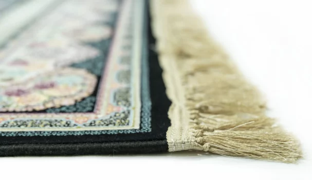 A close-up of a Qaleen Carpets rug with a fringe, featuring a floral pattern and a border, on a white background