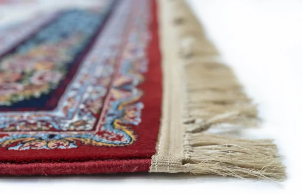 A close-up of a rug's edge, with a red carpet's intricate design and a white border, showcasing the beauty of carpets and